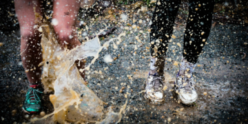 Duas pessoas correndo com o tênis sujo pisando em uma poça de água